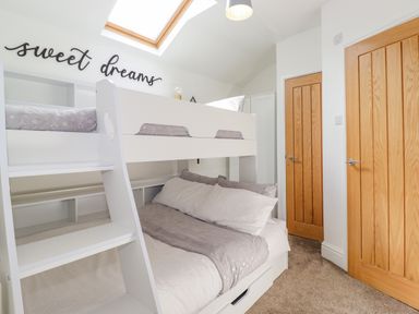 A bedroom with a white bunk bed and wooden doors at Chestnuts Cottage in Windermere