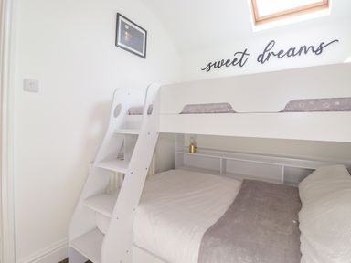 A small bedroom with a white bunk bed a ladder and a skylight window at Chestnuts Cottage in Windermere