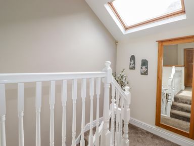 A staircase with white railings a mirror on the wall and a skylight window at Chestnuts Cottage in Windermere