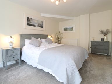 A bedroom with a bed bedside tables dresser and wall art at Chestnuts Cottage in Windermere