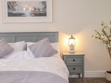 A bedroom with a bed, bedside table with a lamp, and a potted plant at Chestnuts Cottage in Windermere