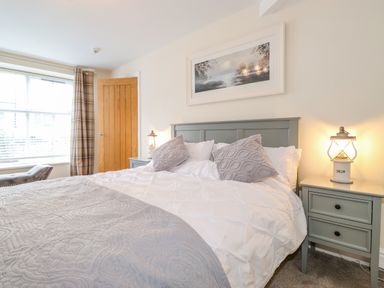 A bedroom with a double bed side tables and a window with plaid curtains at Chestnuts Cottage in Windermere