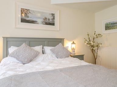 A bedroom with a bed featuring gray pillows and bedding a gray headboard a bedside table with a lantern light and a branch with white flowers at Chestnuts Cottage in Windermere