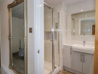 A bathroom with a glass shower enclosure a sink with cabinets and a large mirror and a decorative full length mirror outside the door at Chestnuts Cottage in Windermere