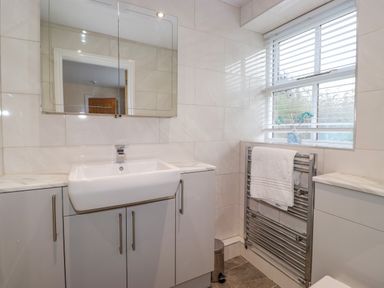 A bathroom with a sink cabinet mirror towel radiator and window at Chestnuts Cottage in Windermere