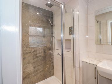 A bathroom with a glass shower enclosure a stone tiled shower wall a white sink and a mirrored cabinet