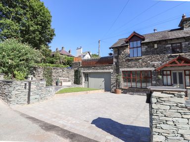 A stone house with a driveway a garage and a small garden with a bench at Chestnuts Cottage in Windermere