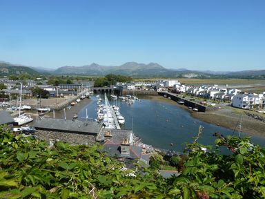A harbor with boats docked along piers surrounded by buildings and mountains in the background at Wenallt in Porthmadog