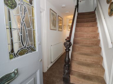 A hallway with a carpeted staircase wooden banister radiator framed pictures and an open door with stained glass at Wenallt in Porthmadog