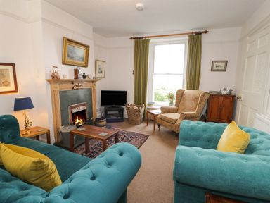 A living room with teal sofas, a fireplace, an armchair, a television, and green curtains at Wenallt in Porthmadog