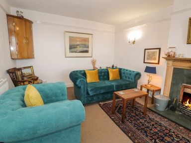 A living room with teal sofas and yellow cushions a wooden coffee table fireplace and wall art at Wenallt in Porthmadog