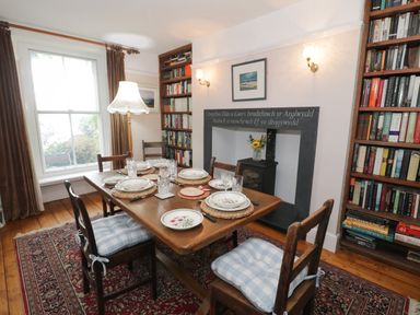 A dining room with a wooden table set with plates and glasses a floor lamp and bookshelves at Wenallt in Porthmadog