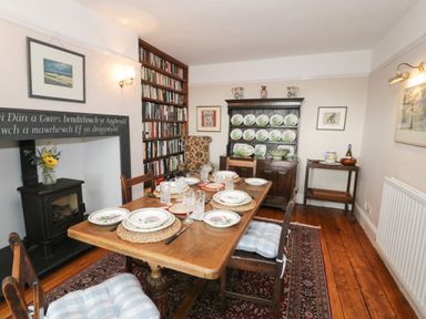 A dining room with a wooden table set for six and a wood burning stove at Wenallt in Porthmadog