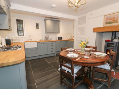 A kitchen with blue cabinets a wooden dining table set for four and a wood stove in the corner at Wenallt in Porthmadog