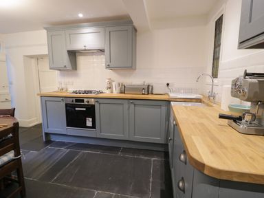 A kitchen with grey cabinets wooden countertops a gas stove oven kettle toaster coffee machine and a sink with a drying rack at Wenallt in Porthmadog
