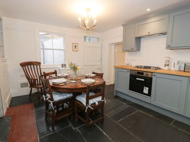 A kitchen with blue cabinets a wooden dining table with chairs and plates at Wenallt in Porthmadog