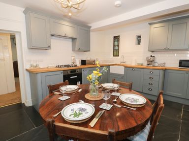 A kitchen with light blue cabinets wooden countertop and a round wooden dining table set with plates glasses and a vase with flowers at Wenallt in Porthmadog