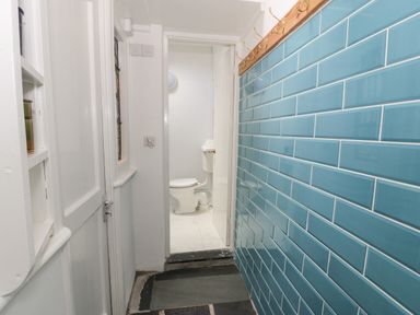 A narrow hallway with white walls and blue tiled wall leading to a bathroom with a toilet at Wenallt in Porthmadog
