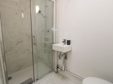 A bathroom shower with glass door a small wall mounted sink and part of a toilet at Wenallt in Porthmadog