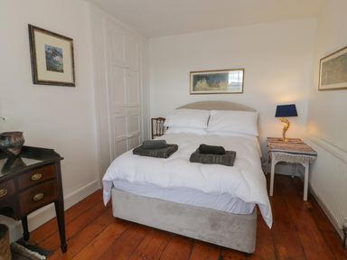 A bedroom with a double bed with white bedding two sets of dark towels two framed pictures a wooden floor a small table with a lamp and a wooden dresser at Wenallt in Porthmadog