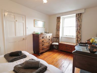 A bedroom with a double bed towels on the bed a wooden chest of drawers a window with floral curtains and a wooden chair at Wenallt in Porthmadog