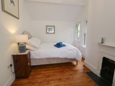 A bedroom with a bed white bedding and blue towels on it a wooden nightstand with a lamp a fireplace and a door with windows at Wenallt in Porthmadog