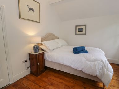 A bedroom with a bed white bedding and rolled towels on the bed a wooden nightstand with a lamp and framed pictures on the walls at Wenallt in Porthmadog