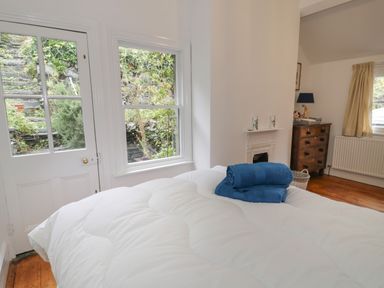 A bedroom with a white bedspread and blue towels on the bed next to a door and window with a view of a garden at Wenallt in Porthmadog
