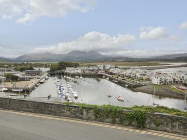 A harbor with boats docked next to buildings and mountains in the background at Wenallt in Porthmadog