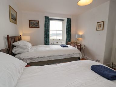 A bedroom with two single beds white bedding a window with curtains and framed pictures on the walls at Wenallt in Porthmadog
