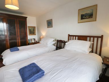 A bedroom with two single beds with white bedding and blue towels a wooden wardrobe and framed pictures on the wall at Wenallt in Porthmadog