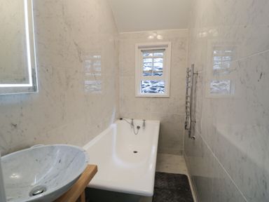A bathroom with a bathtub a marble basin on a wooden stand a towel rack and a small window at Wenallt in Porthmadog
