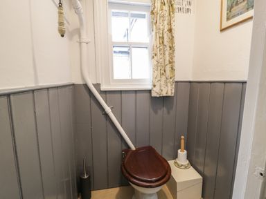A small bathroom with a wooden toilet seat a window with floral curtains and grey wall paneling at Wenallt in Porthmadog