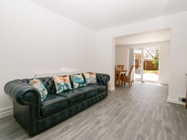 A living room with a black leather sofa and decorative cushions next to a dining area with a wooden table and chairs at Seacider in Burnham-On-Sea