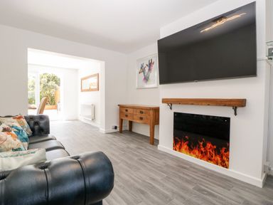 A living room with black leather sofa colorful cushions wooden sideboard wall mounted television and electric fireplace at Seacider Burnham-On-Sea