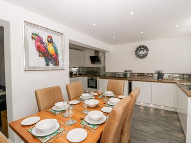 A dining area with six place settings and a kitchen with white cabinets and a wall clock at Seacider in Burnham-On-Sea