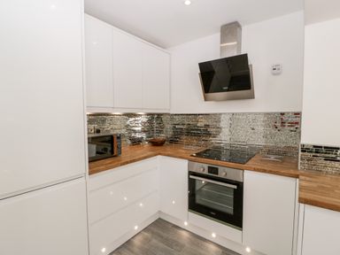 A kitchen with white cabinets wooden countertops a black oven and stovetop a microwave and a metallic backsplash at Seacider in Burnham-On-Sea