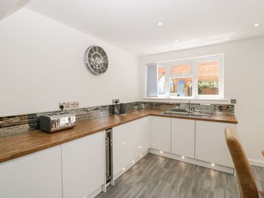 A kitchen with white cabinets wooden countertop a sink toaster kettle wall clock and window at Seacider in Burnham-On-Sea