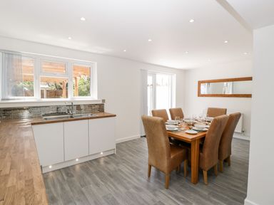 A kitchen and dining area with wooden countertops and a dining table with six chairs set with plates and glasses at Seacider in Burnham-On-Sea