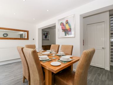 A dining room with a wooden table set for six people with beige chairs and colorful bird paintings at Seacider in Burnham-On-Sea