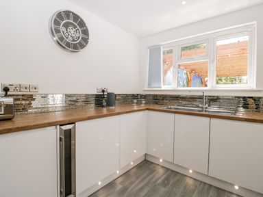 A kitchen with white cabinets wooden countertops a large clock on the wall and a window above the sink at Seacider in Burnham-On-Sea