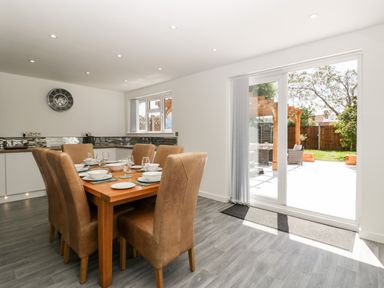 A dining area with a wooden table and six brown chairs next to a kitchen and sliding glass doors leading to a garden at Seacider in Burnham-On-Sea