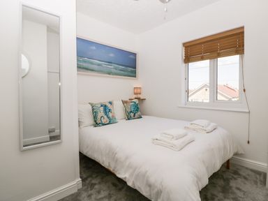 A bedroom with a double bed white bedding sea themed pillows coastal artwork a mirror and a window with wooden blinds at Seacider in Burnham-On-Sea