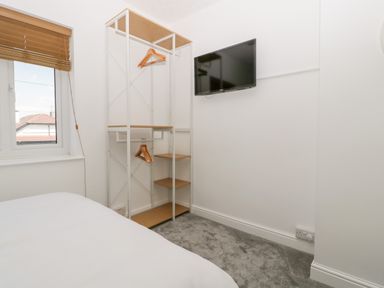 A bedroom with a bed a window with blinds a wall mounted TV and an open wardrobe with hangers at Seacider in Burnham-On-Sea