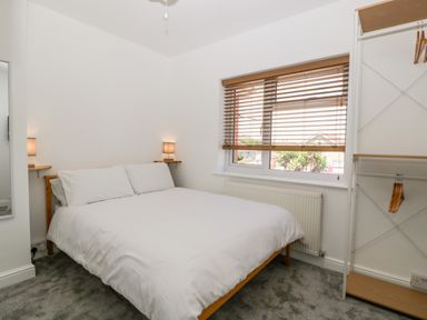 A bedroom with a bed white bedding bedside shelves with lamps window with wooden blinds and an open wardrobe at Seacider in Burnham-On-Sea