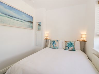 A bedroom with a bed with white bedding and two pillows with sea creature designs two wall lamps and a painting of ocean waves at Seacider in Burnham-On-Sea