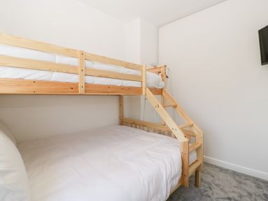 A bedroom with a wooden bunk bed white bedding and a mounted television at Seacider in Burnham-On-Sea