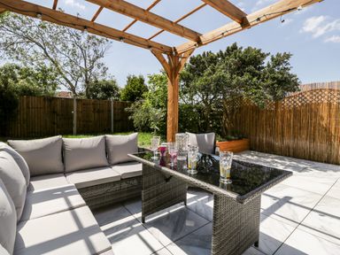 An outdoor patio with a wicker sectional sofa and glass table under a wooden pergola at Seacider in Burnham-On-Sea