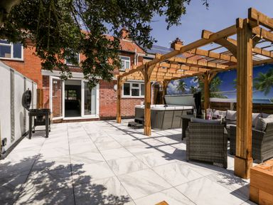 An outdoor patio area with tiled flooring a wooden pergola a hot tub wicker furniture and a barbecue grill at Seacider in Burnham-On-Sea