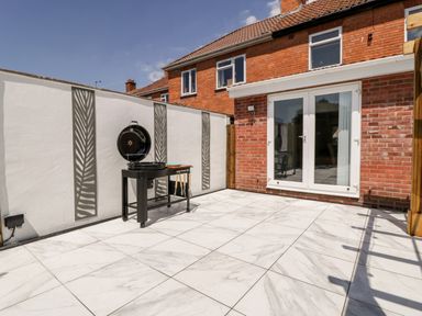 An outdoor patio area with a barbecue grill and white tiled flooring at Seacider in Burnham-On-Sea